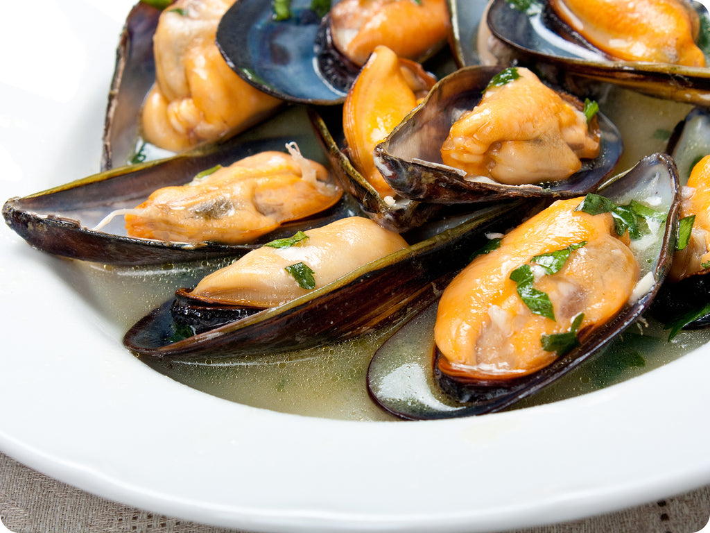 Mediterranean Mussels prepared in a broth with herbs, served in a white bowl.