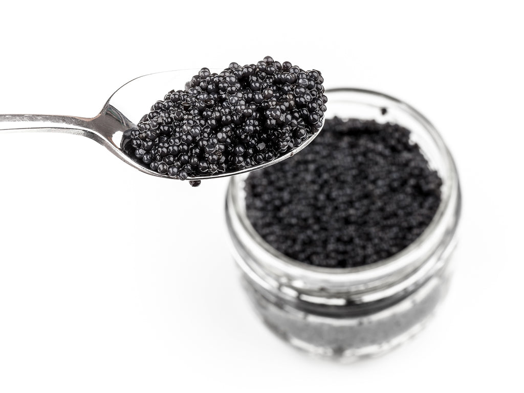 A silver spoon filled with caviar is taken from a glass jar of Paddlefish Roe.
