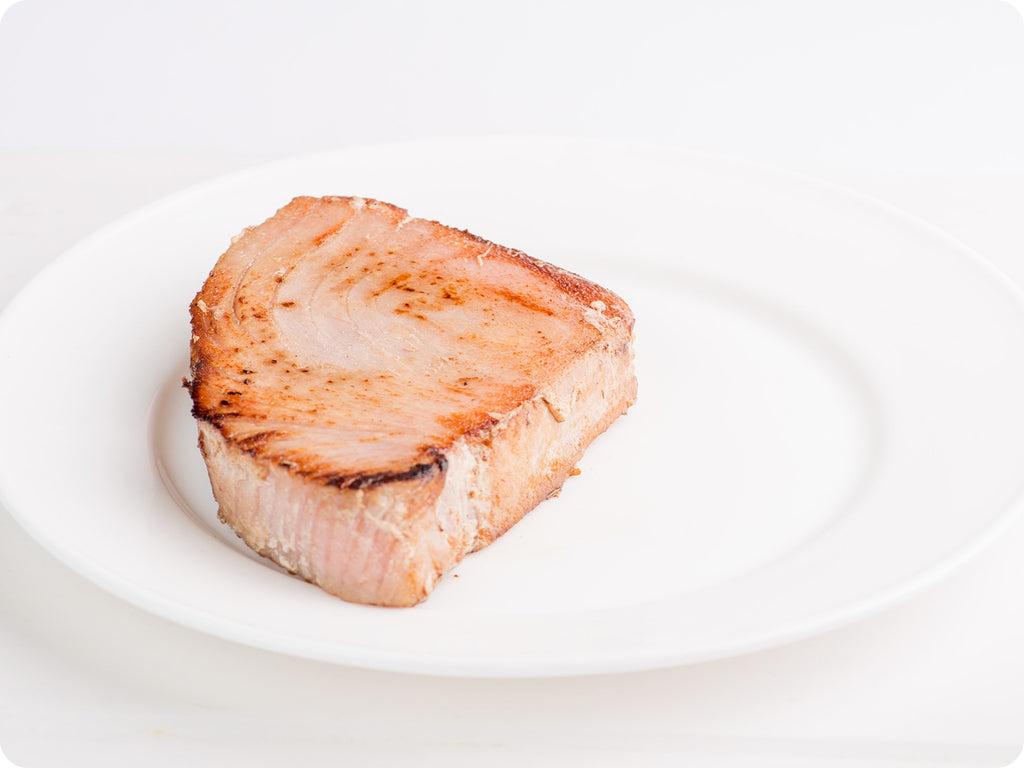 A grilled wild Tombo Tuna steak on a white plate.
