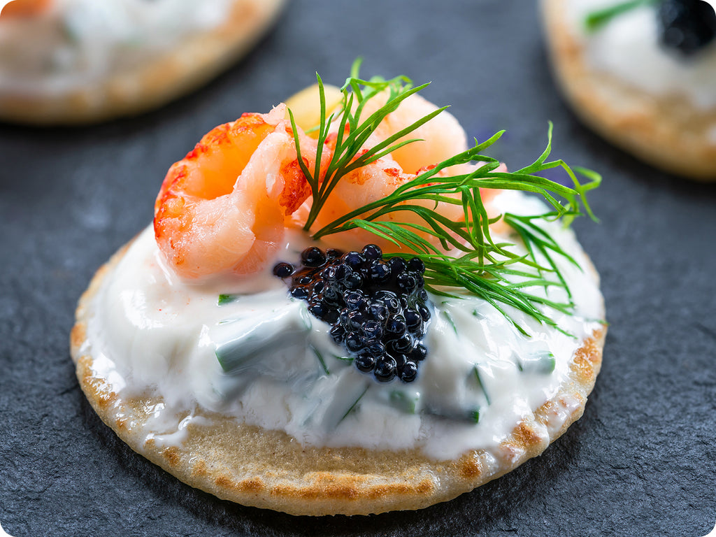 Blini appetizer served with cold smoked salmon,  crème fraiche, Beluga caviar, and fresh dill. 