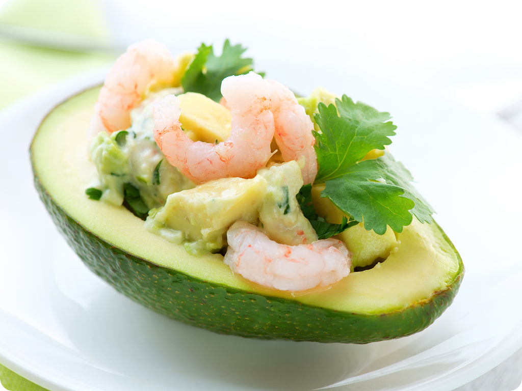 Northern Shrimp are mixed with diced avocado and seasoning, served in half of an avocado on a small white plate.