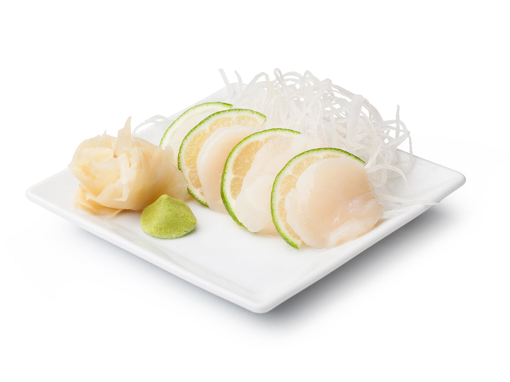 Wild Sea scallops are served sashimi style between slices of lime, plated with rice noodles, fresh ginger, and wasabi.