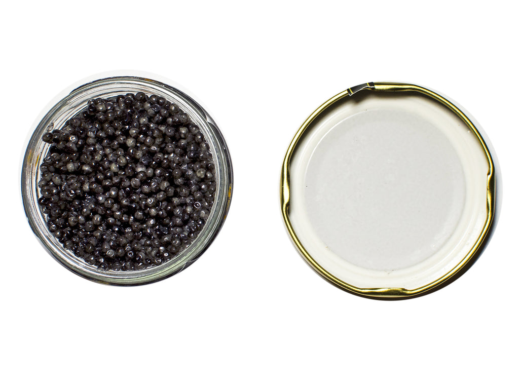 An arial shot of Sevruga Caviar in a glass jar with gold lid to the side.