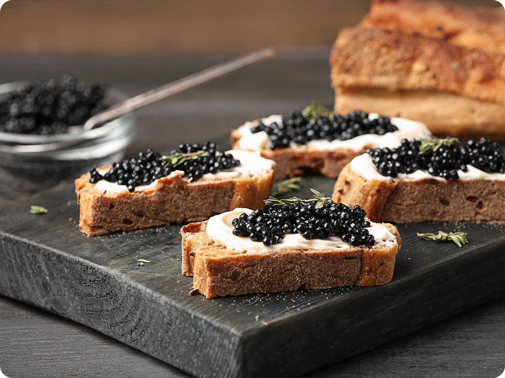 A dark grey wood cheese board, serves slices of fresh bread with creme fraise and Sevruga Caviar.